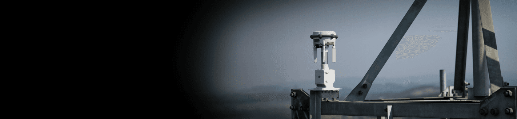 En DJI D-RTK 3 monterad på en metallstruktur med en suddig landskapsbakgrund.