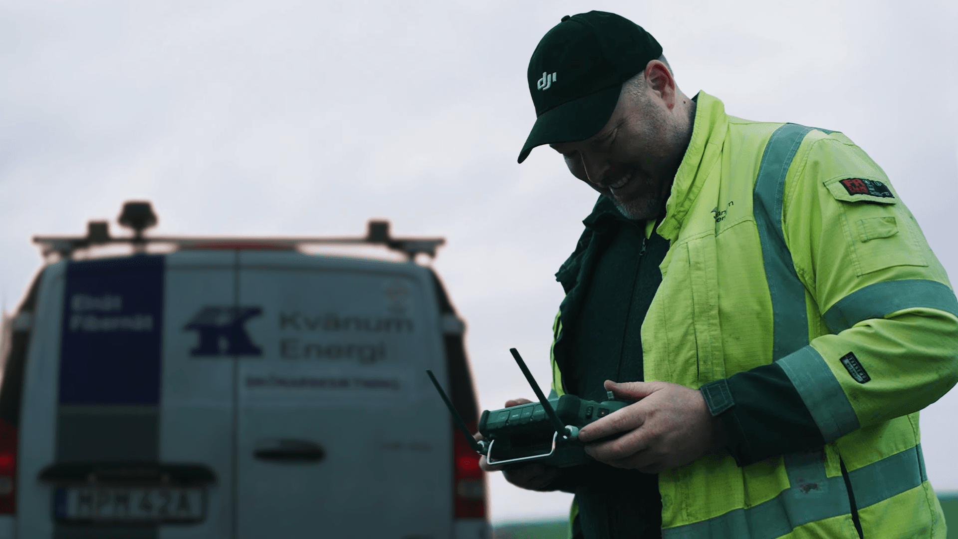 En person i arbetskläder hanterar en fjärrkontroll framför en servicebil med företagslogotyp.