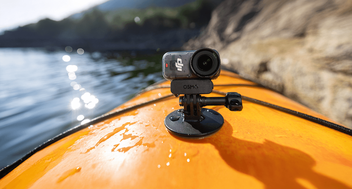 En DJI Osmo Nano monterad på en orange kajak, med glittrande vatten och klippor i bakgrunden.