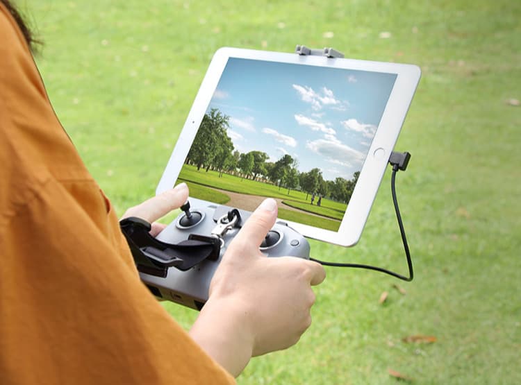 "En fjärrkontroll med en monterad surfplatta visas i olika vinklar för att demonstrera ergonomisk användning. En person håller fjärrkontrollen utomhus med en lanyard för extra stöd."