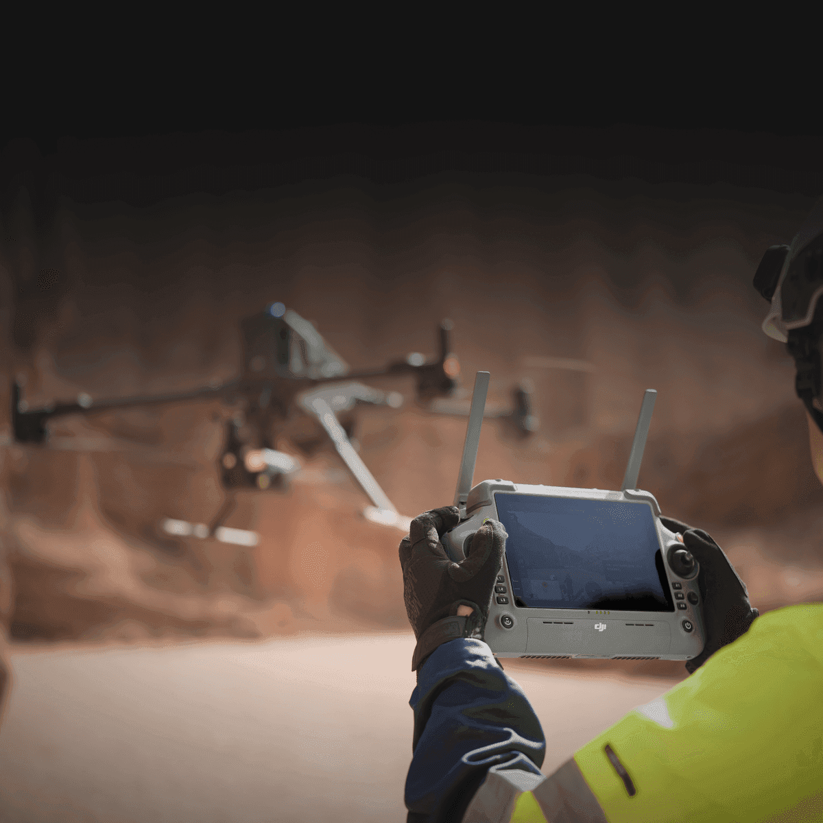 En person styr en drönare med en fjärrkontroll i en ökenliknande miljö.