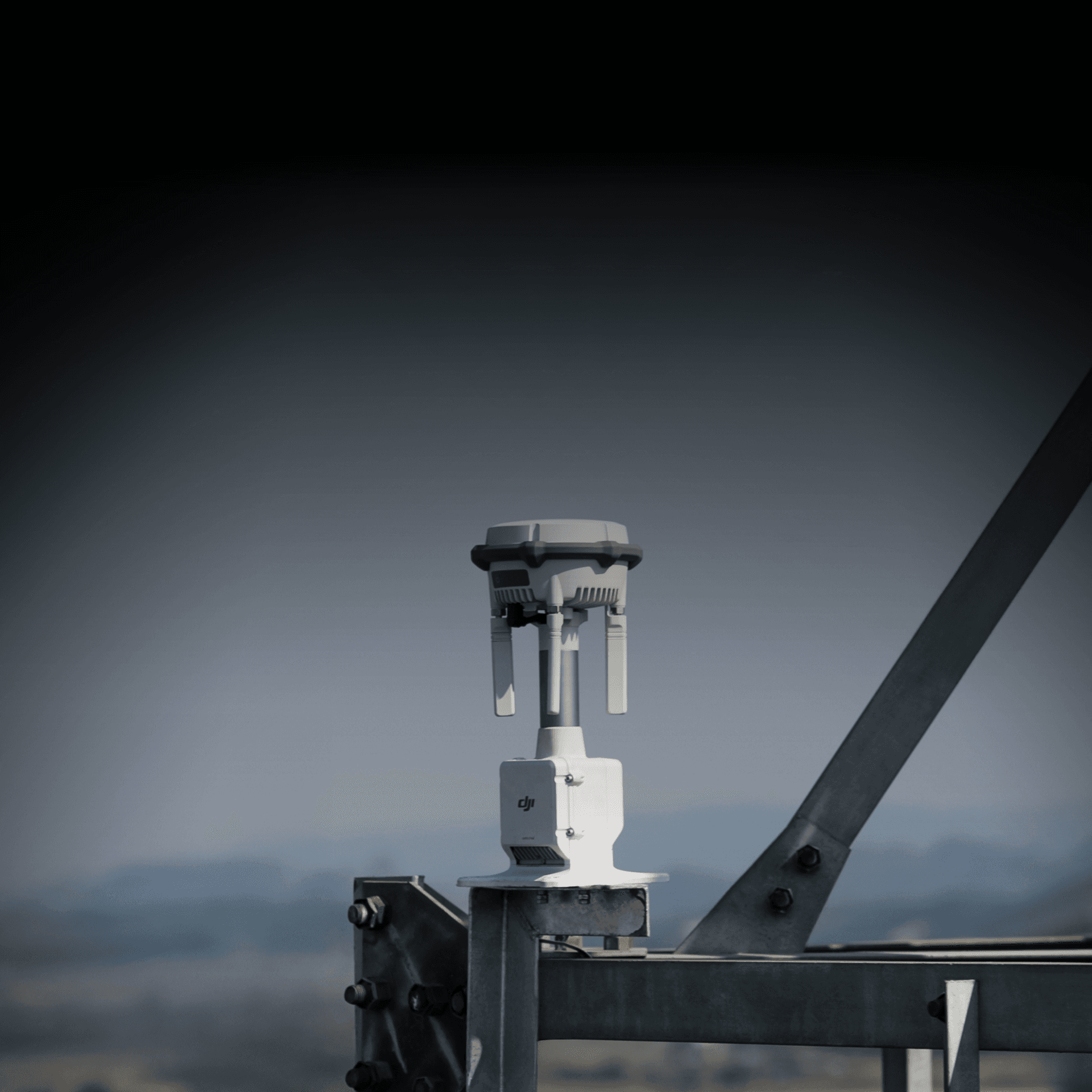 En DJI D-RTK 3 monterad på en metallstruktur mot en suddig bakgrund av landskap.