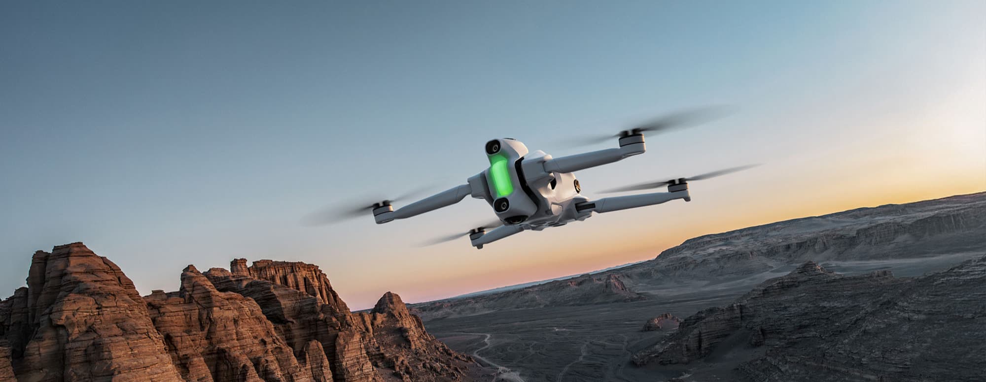 En drönare svävar över ett dramatiskt ökenlandskap med klippformationer i solnedgångens ljus.