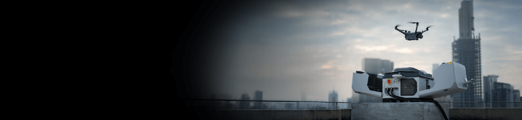En drönare lyfter från en landningsstation på ett tak med en stadssilhuett i bakgrunden.