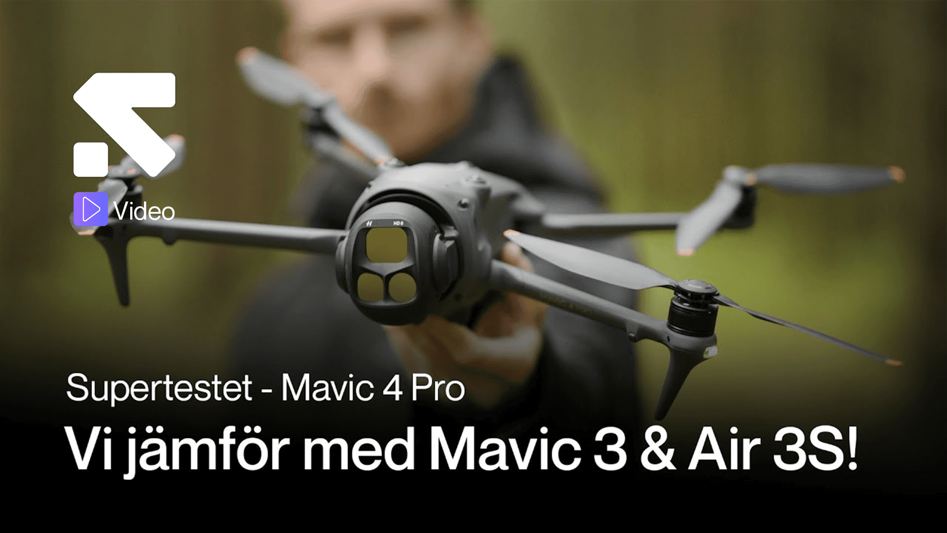 En person håller en Mavic 4 Pro-drönare i fokus, redo för jämförelse med andra modeller i en skogsmiljö.