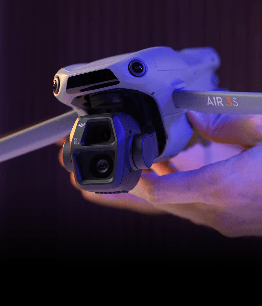 En person håller en avancerad drönare med dubbla kameror mot en mörk bakgrund.