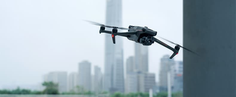 En DJI Mavic 3 Thermal Advanced (M3TA) drönare svävar framför en stadssilhuett med höga byggnader i bakgrunden.