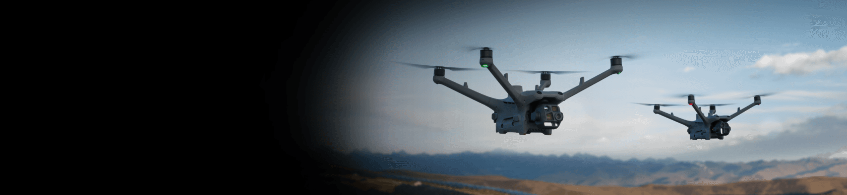 Två drönare svävar i luften över ett bergigt landskap under en klar himmel.