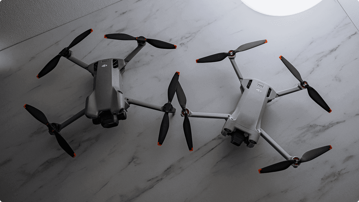 Två moderna drönare med fyra propellrar vardera ligger på en marmorerad yta, redo för flygning.