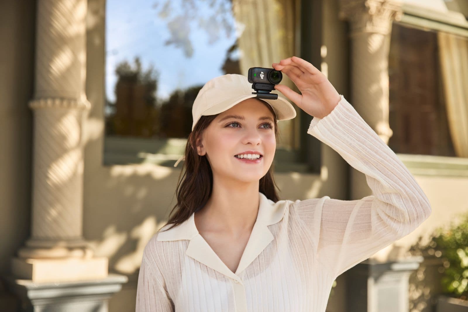 En person bär en keps med en liten DJI Osmo Nano monterad ovanpå, stående utomhus framför en byggnad.