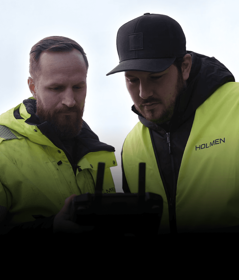 Två personer i gula jackor tittar på en fjärrkontroll utomhus.