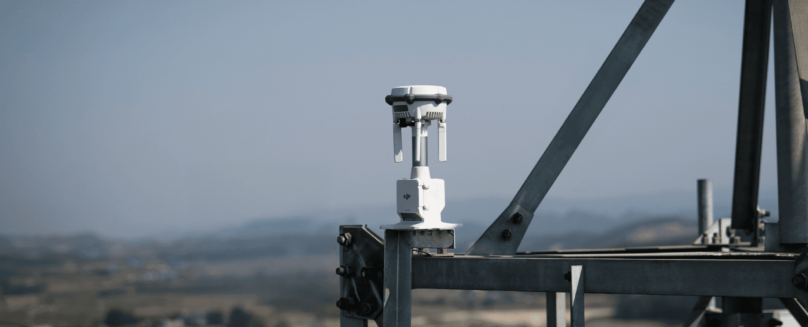 En teknisk sensor monterad på en metallstruktur med en suddig landskapsbakgrund.