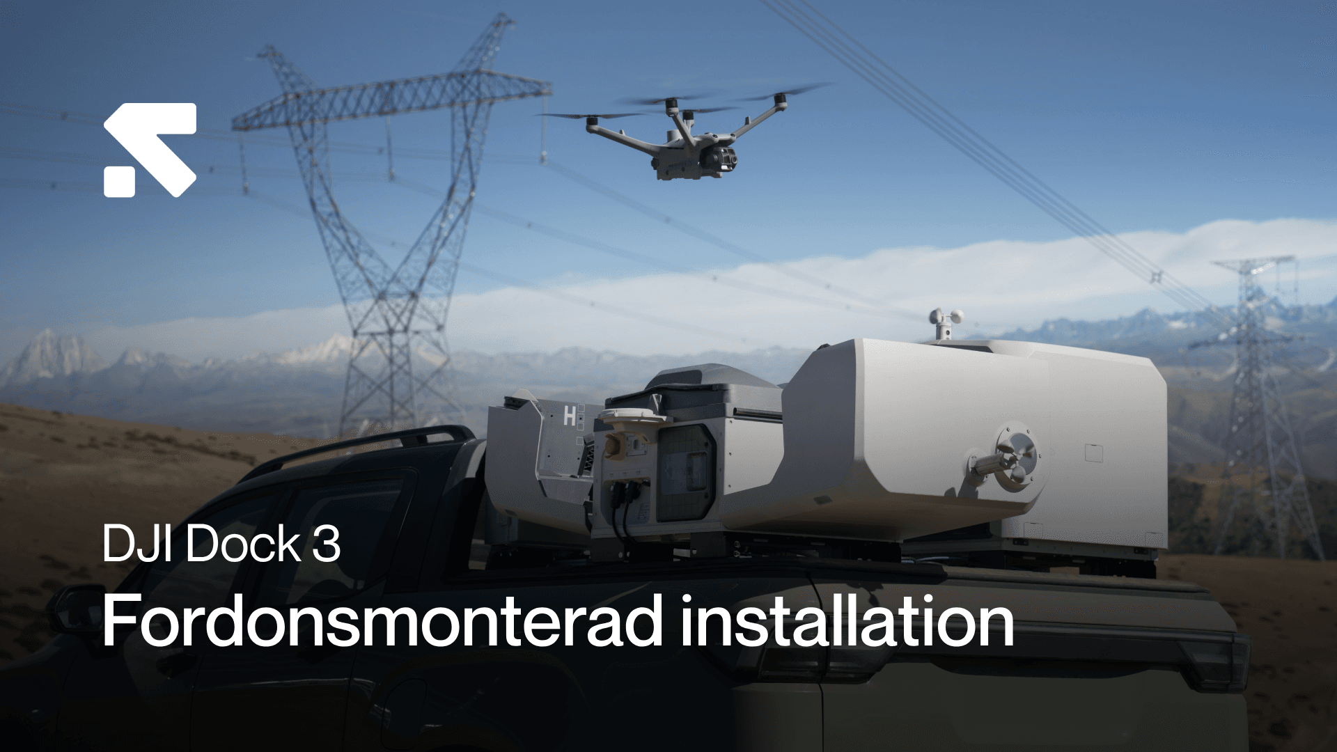 En drönare flyger nära en fordonmonterad DJI Dock 3-installation i ett landskap med kraftledningar och berg i bakgrunden.