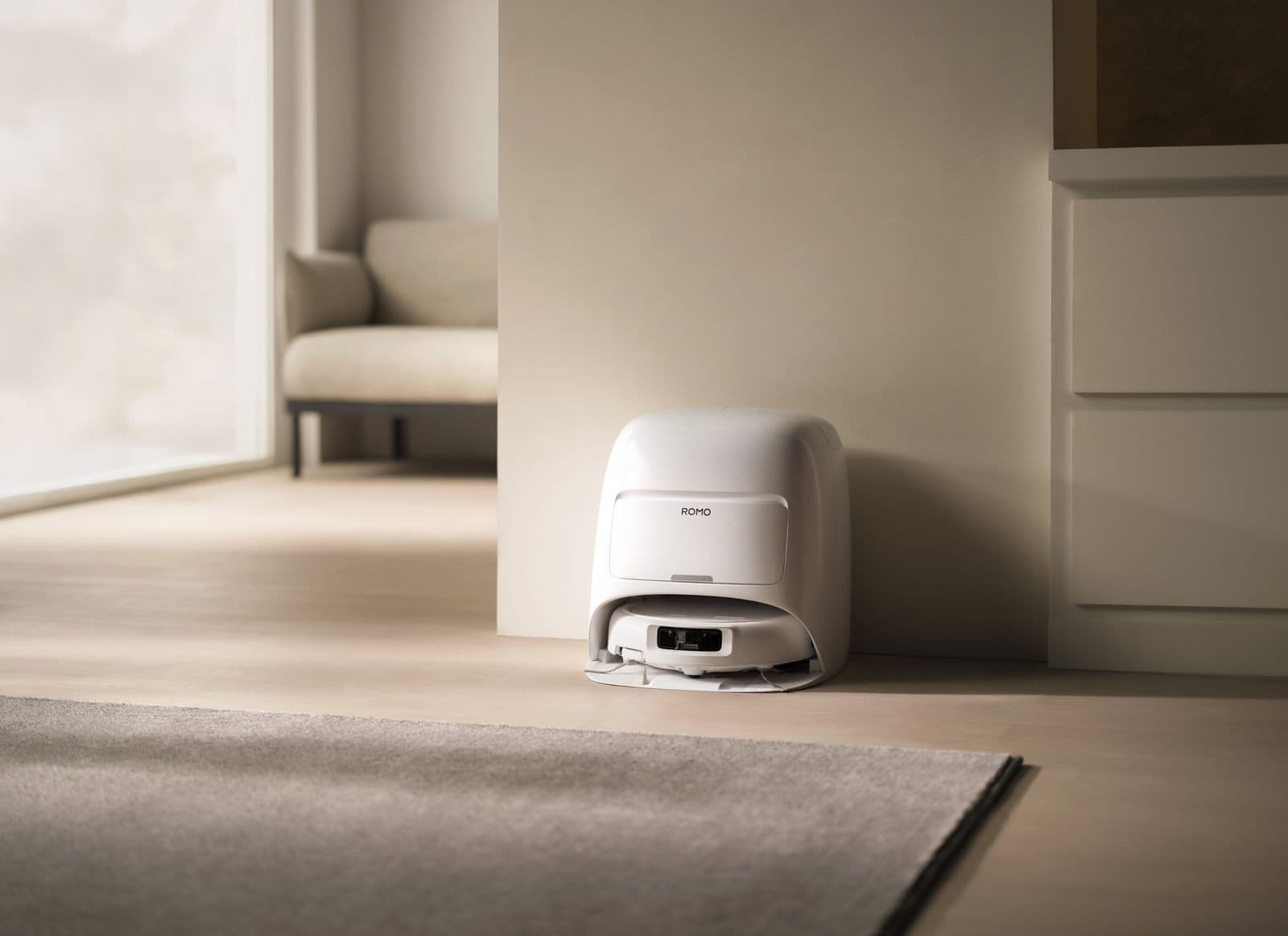 En robotdammsugare laddas i sin station i ett modernt och minimalistiskt vardagsrum.