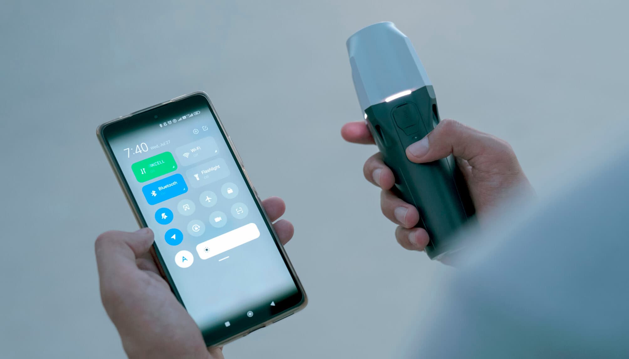 En person håller en smartphone med kontrollpanelen öppen och en Emlid Reach RX i andra handen.