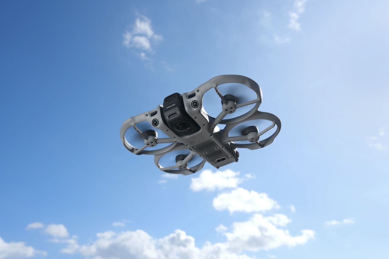 En modern DJI Avata 360-drönare svävar i en klarblå himmel, redo för flygfotografering.