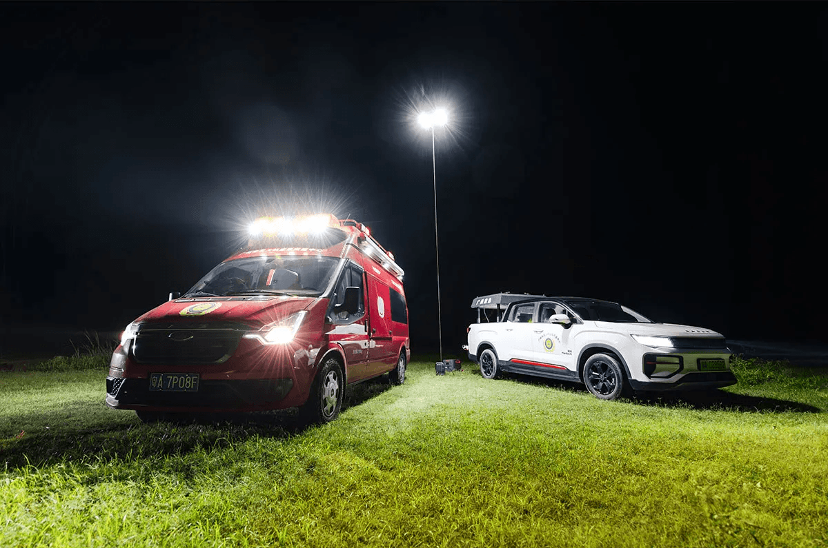 Två utryckningsfordon, en röd skåpbil och en vit SUV, står upplysta på en gräsyta av CZ10 Tethered Hover Light.