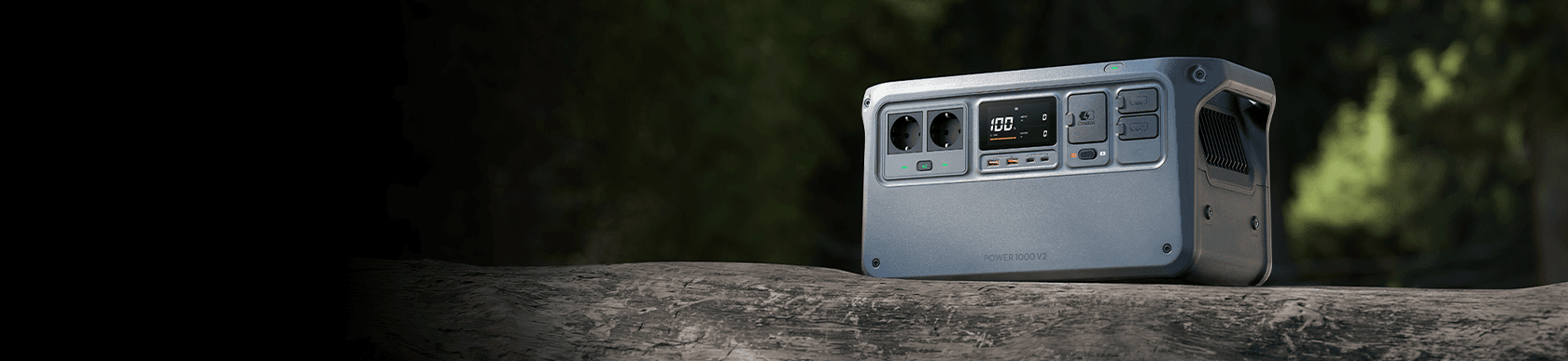 En bärbar kraftstation placerad på en träyta i en utomhusmiljö, omgiven av grönska.