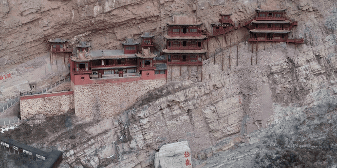 En serie traditionella byggnader klamrar sig fast vid en brant klippvägg, vilket skapar en dramatisk och historisk vy.