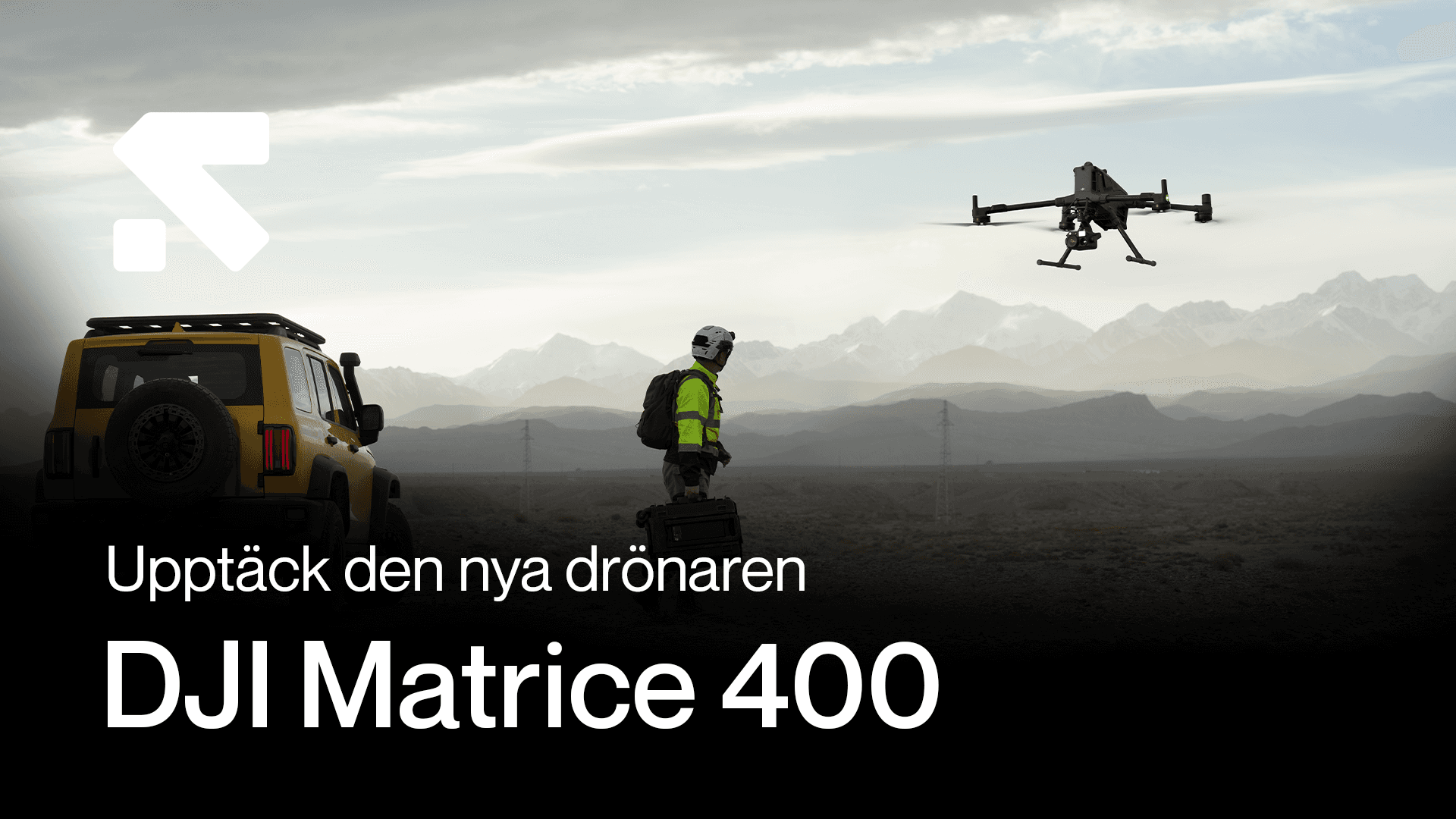 En person i skyddsutrustning och varselställ står bredvid en gul bil i ett ökenlandskap och observerar en DJI Matrice 400 i luften.