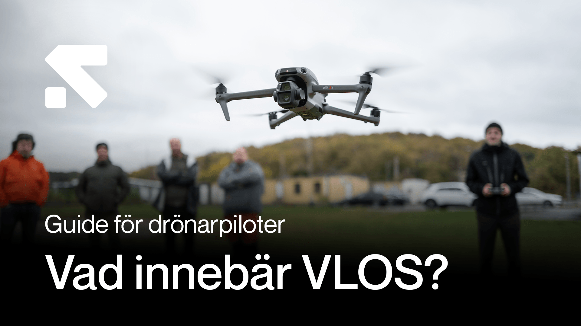 En drönare svävar i luften medan flera personer står i bakgrunden på en gräsyta, med texten 'Guide för drönarpiloter: Vad innebär VLOS?' i förgrunden. en-dronare-svavar.png