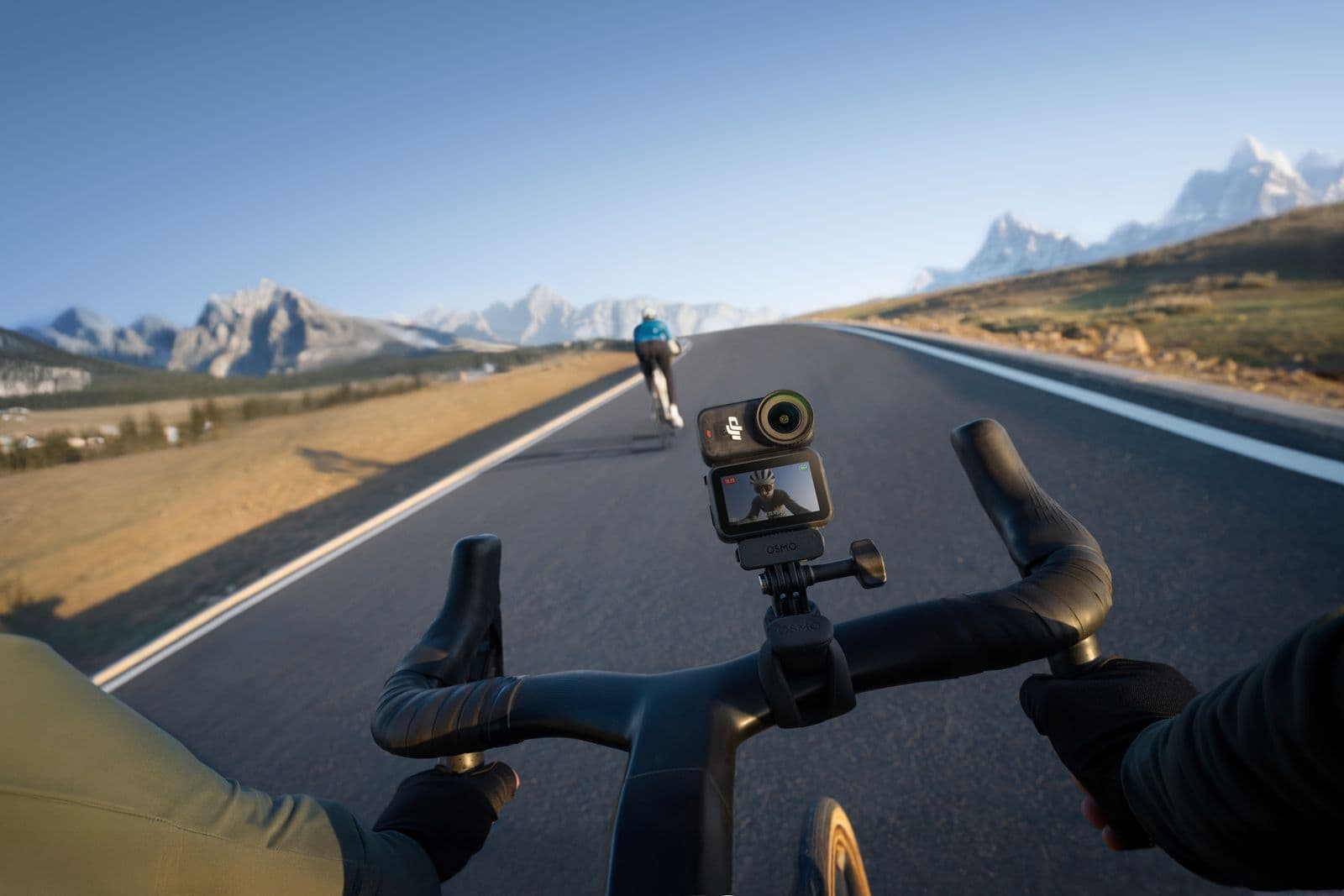 En cyklist filmar sin tur med en DJI Osmo Nano monterad på styret, medan de cyklar uppför en landsväg med berg i bakgrunden.