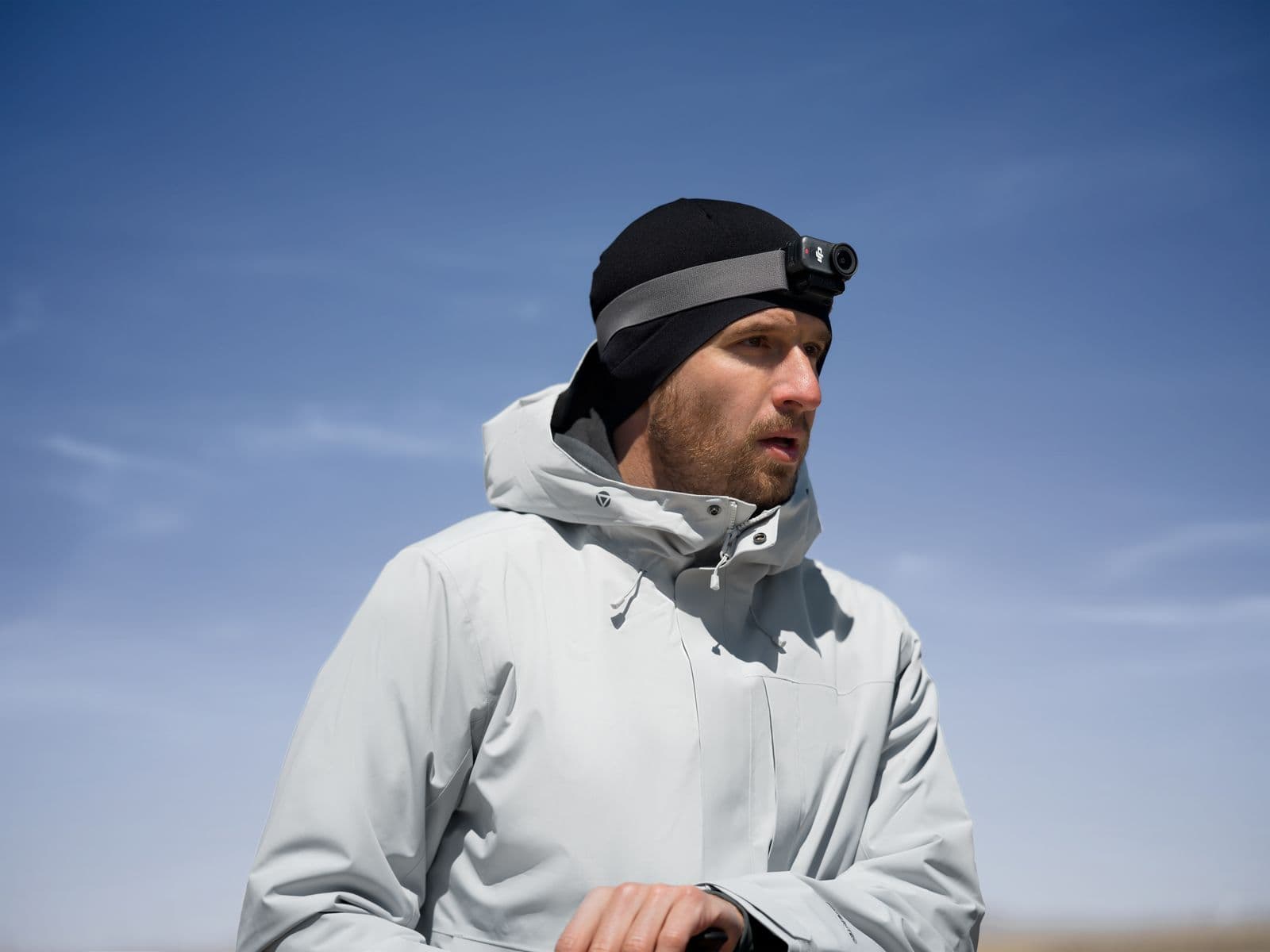 En person i vinterjacka och mössa med en DJI Osmo nano fäst på huvudet står utomhus under en klarblå himmel.