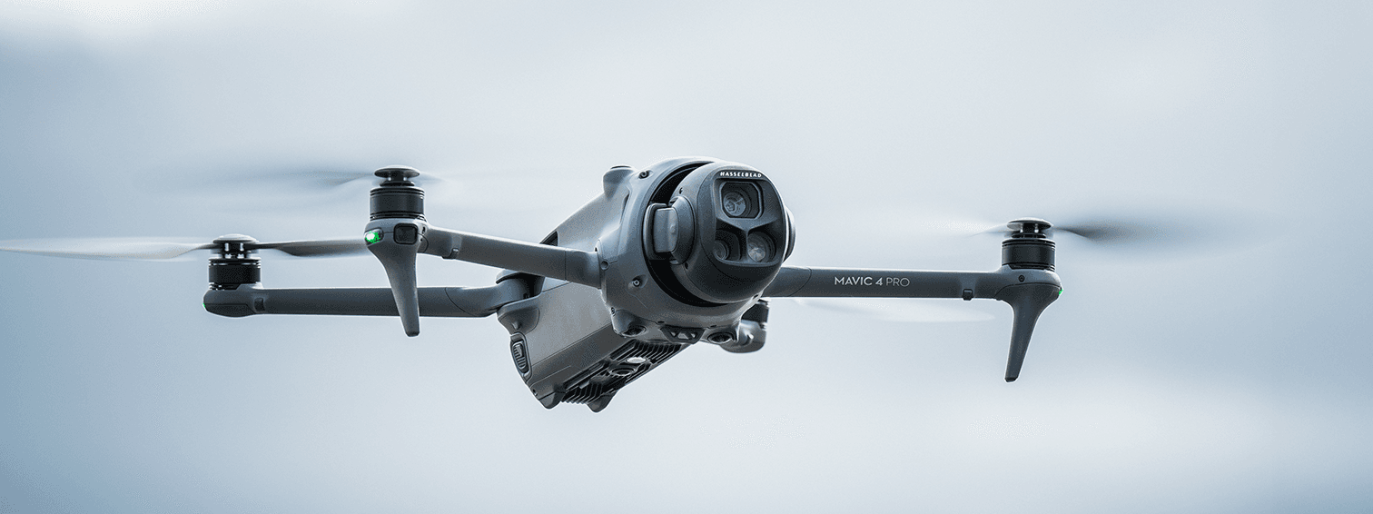 En Mavic 4 Pro svävar i luften mot en klar himmel, med sina rotorblad i rörelse.