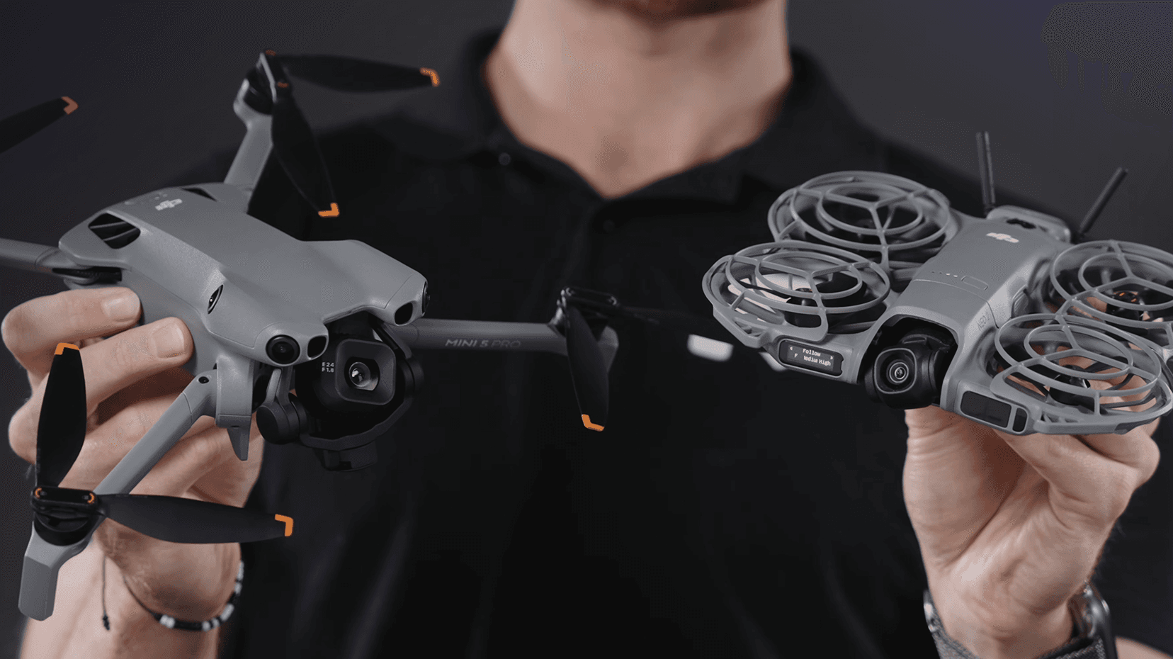 En person håller två avancerade drönare, en DJI Mini 5 Pro med öppna propellrar och en DJI Neo 2 med skyddade propellrar, mot en mörk bakgrund.