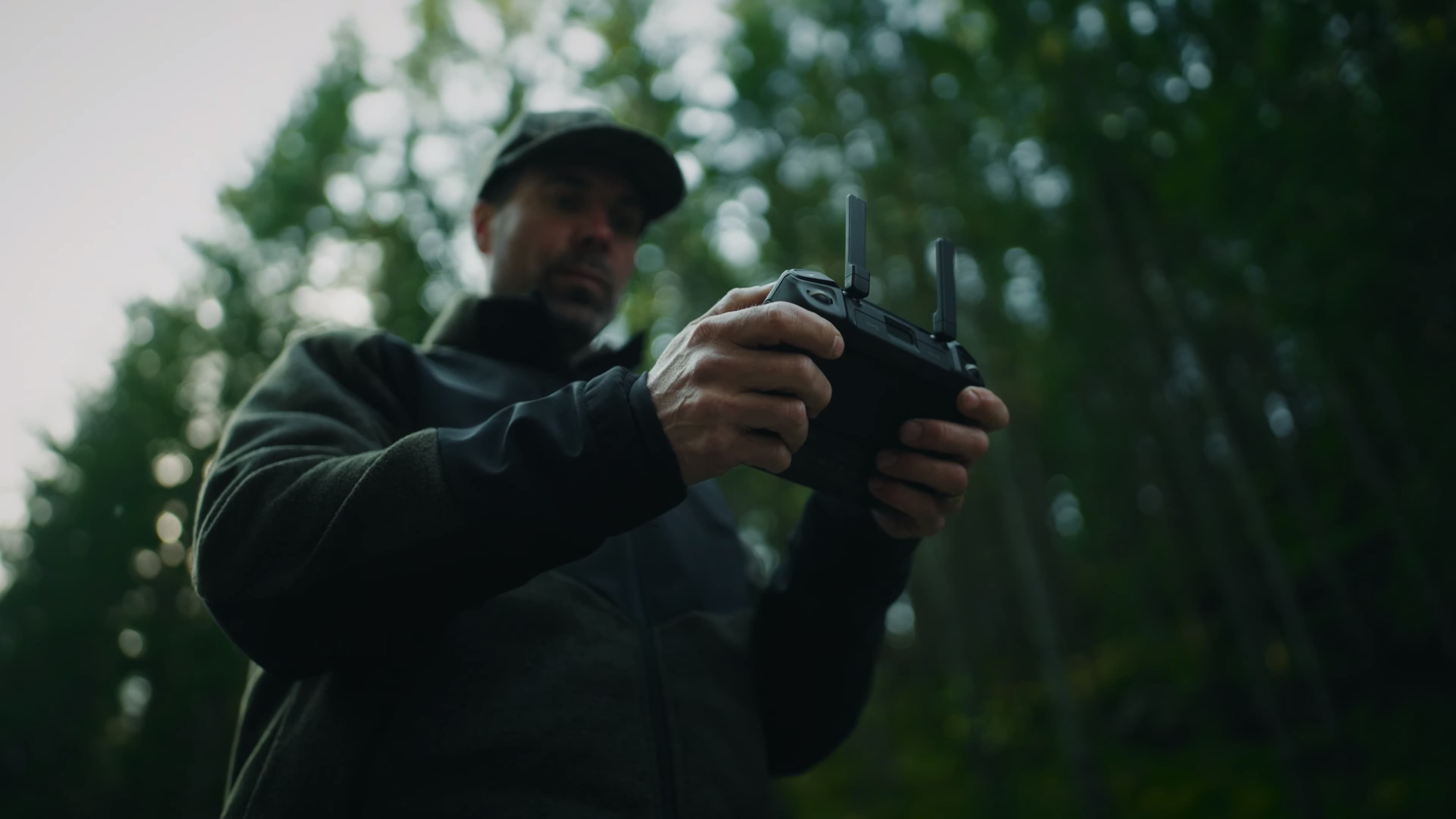 En person styr en drönare med en fjärrkontroll i en skogsmiljö.