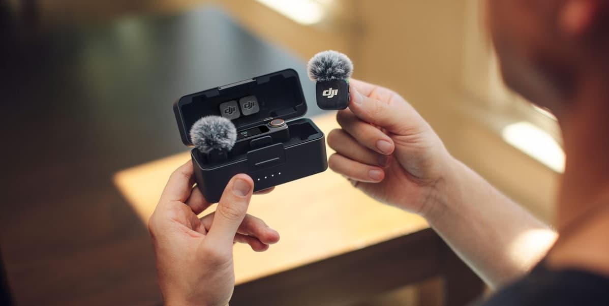 En person håller i en trådlös mikrofon och laddningsetui i ett solbelyst rum.