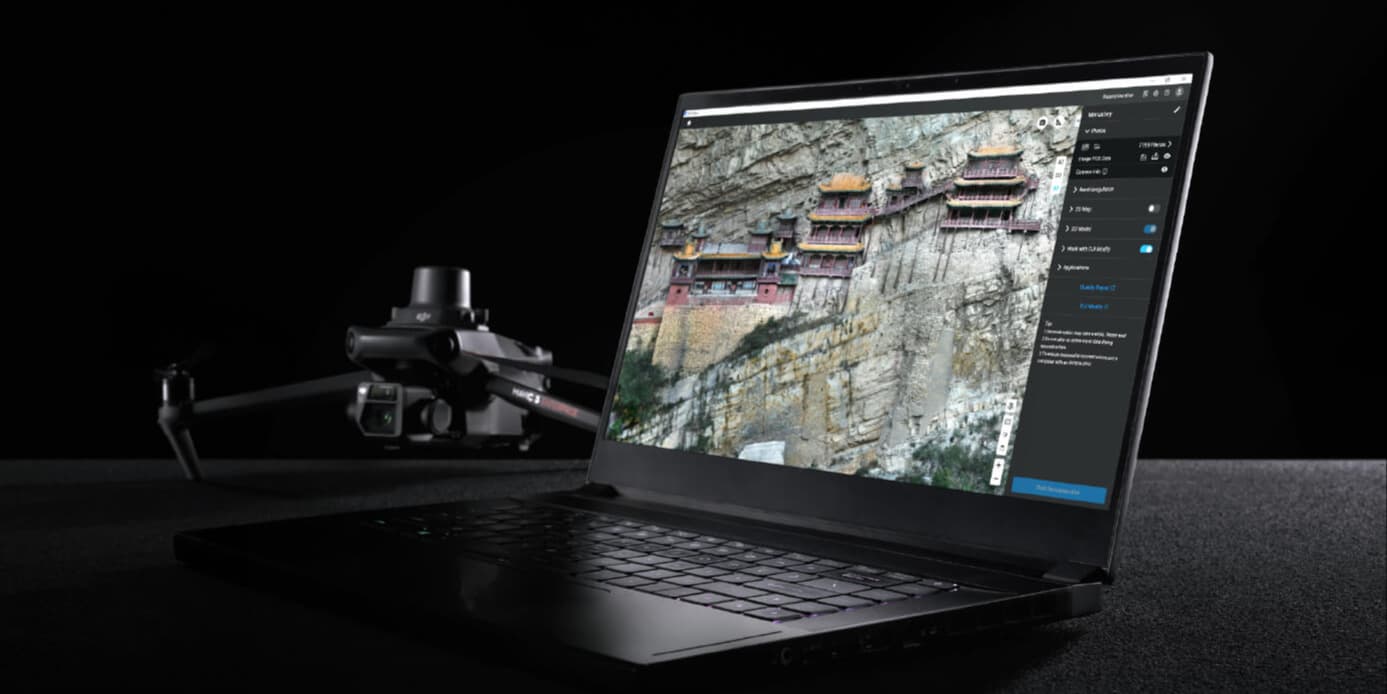 En bärbar dator visar en detaljerad bild av ett kloster på en klippa, medan en drönare står redo i bakgrunden på en mörk yta.
