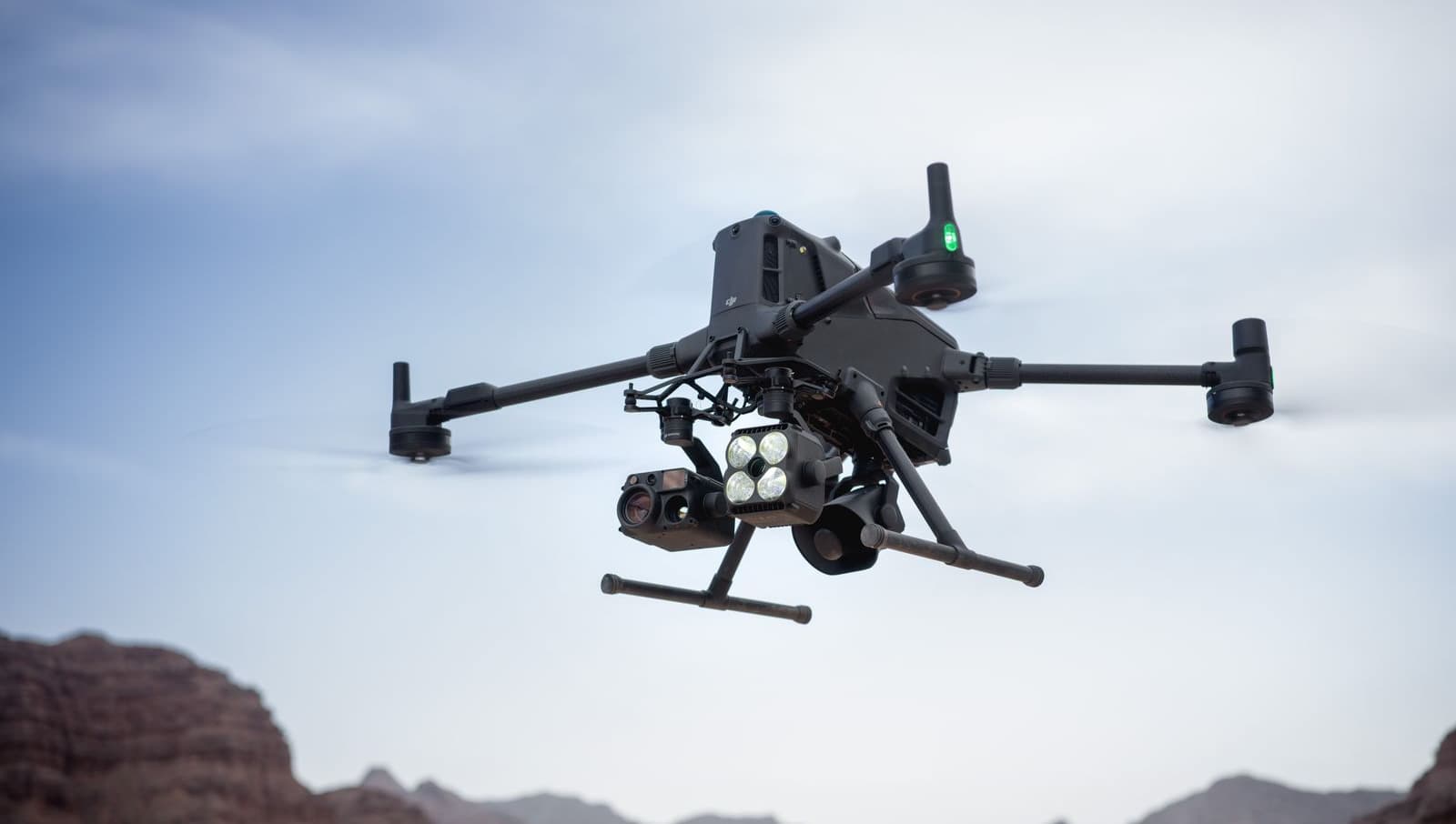 En avancerad DJI Matrice 400 svävar över ett ökenlandskap med berg i bakgrunden.