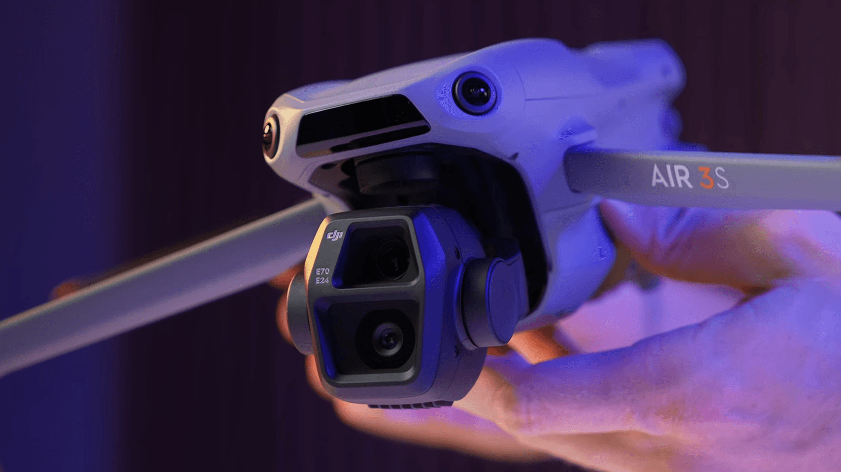 En närbild av en avancerad drönare med dubbla kameror, hålls i handen under en lila bakgrundsbelysning.