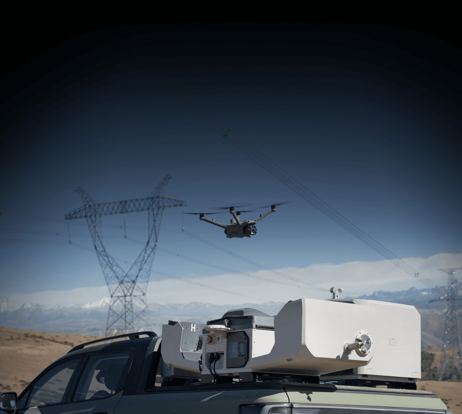 En drönare svävar nära kraftledningar i ett ökenlandskap, med avancerad utrustning monterad på ett fordon i förgrunden.