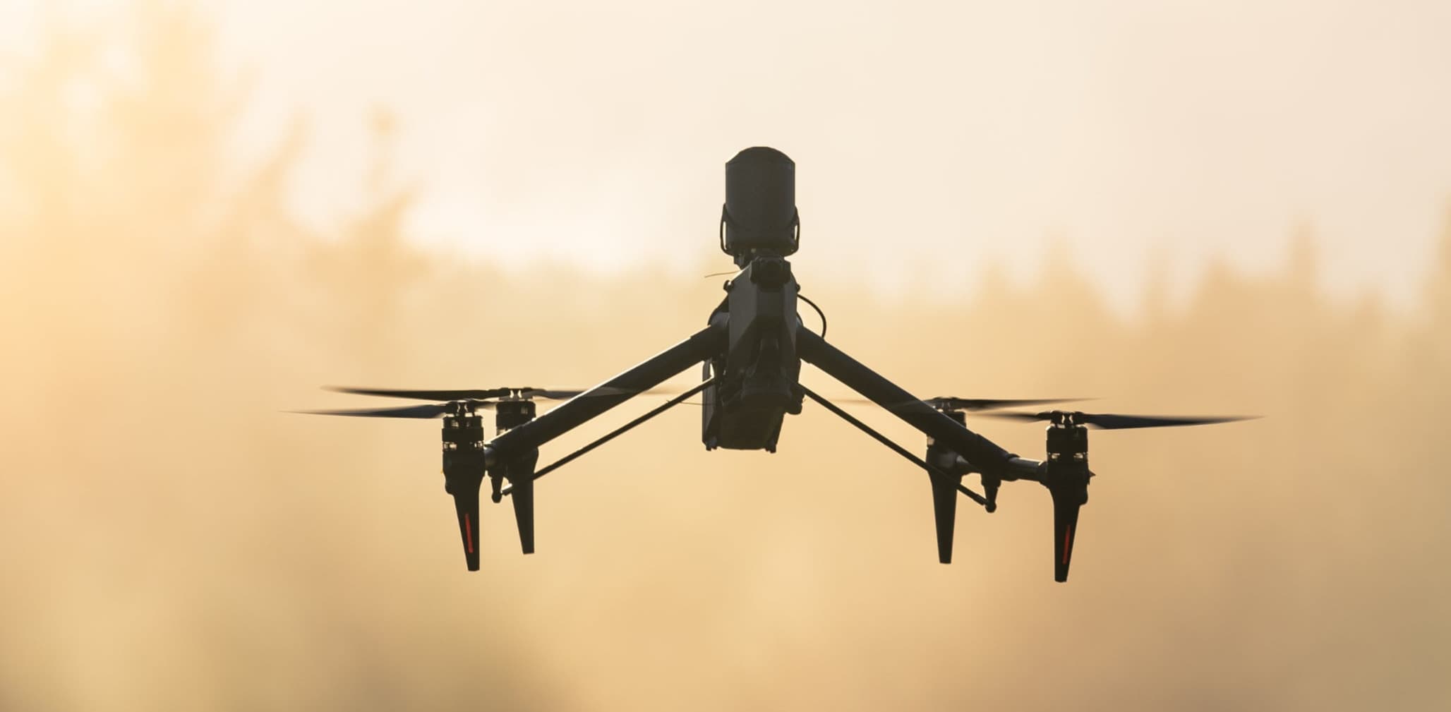 "En drönare svävar i luften mot en dimmig skogsbakgrund i gryningsljus."