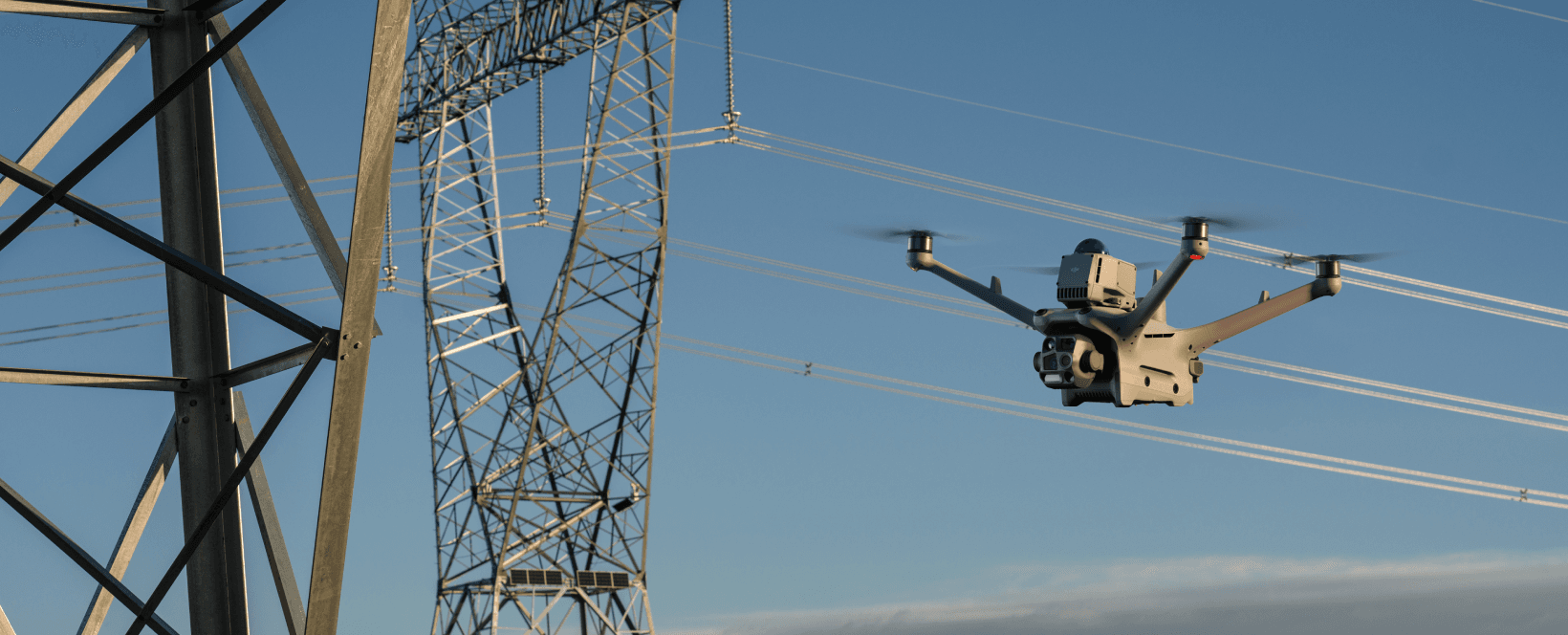En drönare flyger nära kraftledningar och torn under en klar himmel.