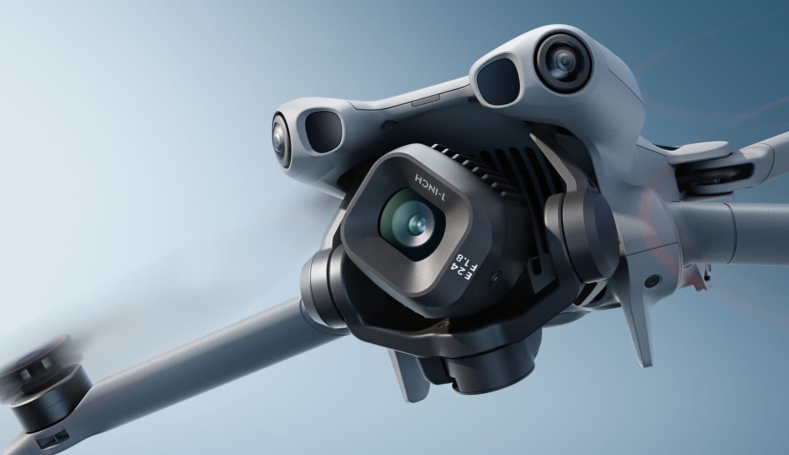 En närbild av en avancerad drönare med flera kameror och roterande propellrar mot en blå bakgrund.